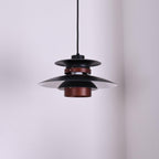 A black Clérachic pendant hangs in a plain corner room, seen from below.