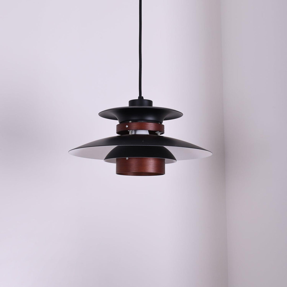 A black Clérachic pendant hangs in a plain corner room, seen from below.