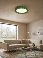 This Clérachic ceiling light in green lights a living room with a beige sofa and a large window overlooking a city park.