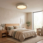 This Clérachic ceiling light in white lights a bedroom with a wooden bed frame, linen bedding and an olive tree.