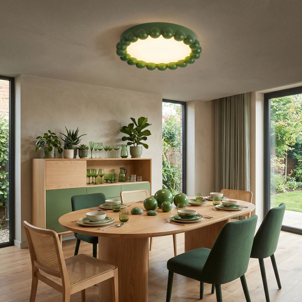 This Clérachic ceiling light in green lights an oval dining table set for a meal, beside sliding glass doors to a garden.