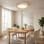 This Clérachic ceiling light, in white with a beaded rim, lights a wooden dining table set in a warm, plant-filled room.