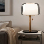 Clérachic lamp lit on a marble side table beside a sofa, its glass shade glowing bright white.