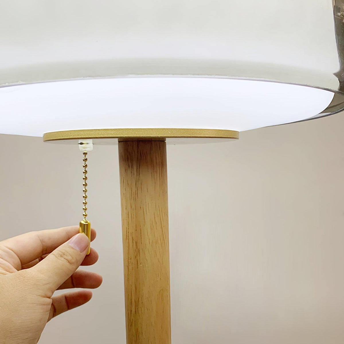 Close-up of the Clérachic lamp's brass disc and pull-cord switch where the oak stem meets its glass shade.