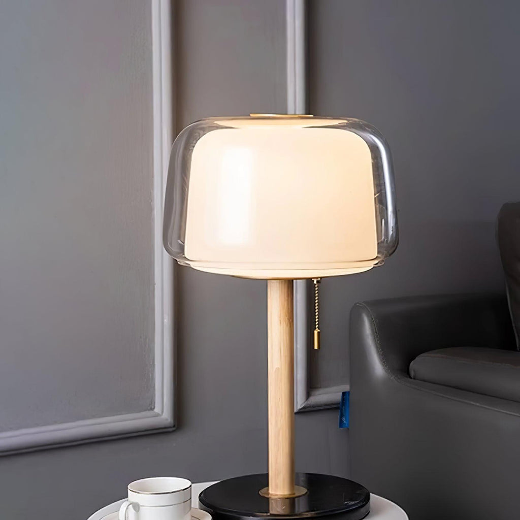 Clérachic lamp lit beside a leather armchair, its glass shade glowing above a cup and saucer on the table below.