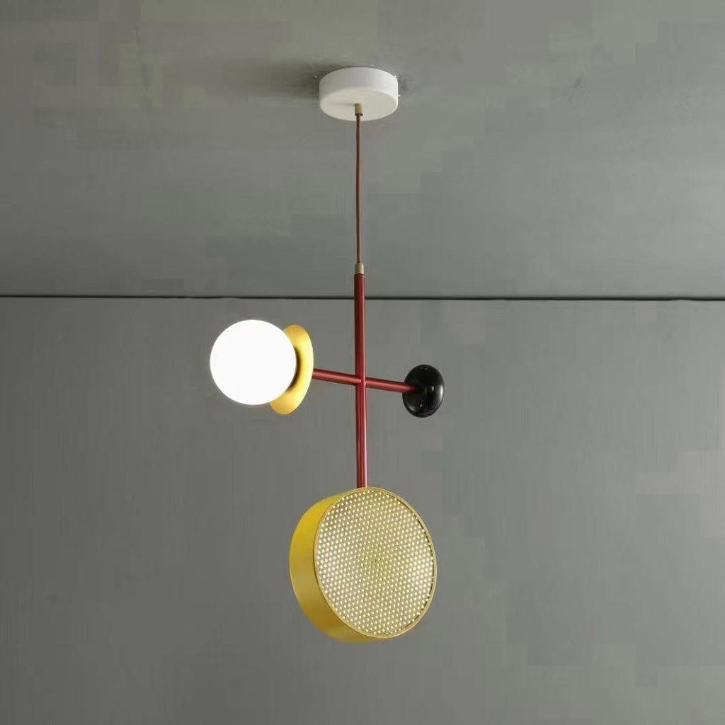 Clérachic pendant with a red rod, gold disc and opal glass globe hanging from a plain grey ceiling and wall.