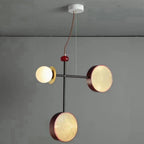 Clérachic pendant with a black rod, one cane drum and one opal glass globe, hanging against a plain grey wall.