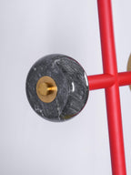 Macro shot of the grey veined marble ball joint where a Clérachic chandelier's red cross-arm meets its brass mounting disc.