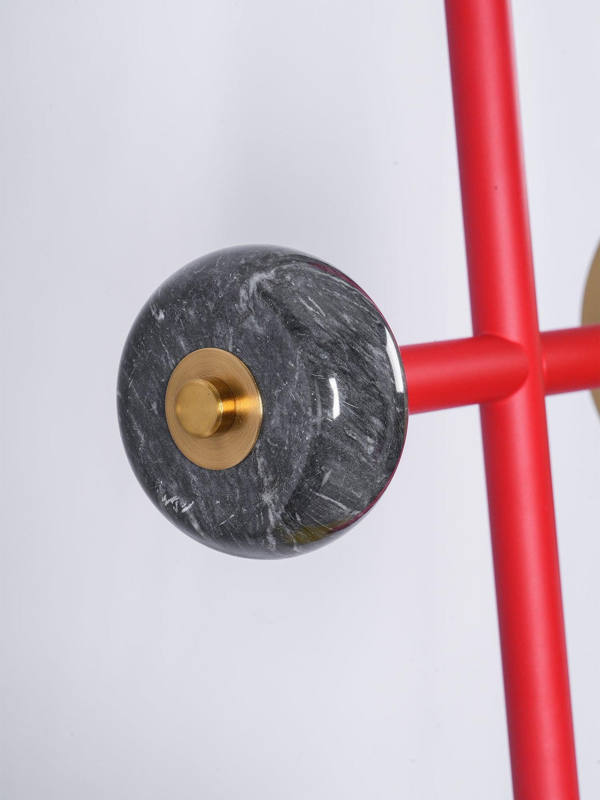 Macro shot of the grey veined marble ball joint where a Clérachic chandelier's red cross-arm meets its brass mounting disc.