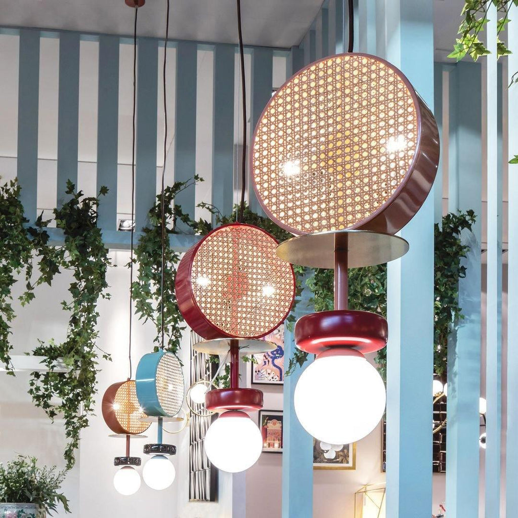 Cluster of Clérachic drum pendants in coral, teal and maroon hanging among trailing plants between striped columns.