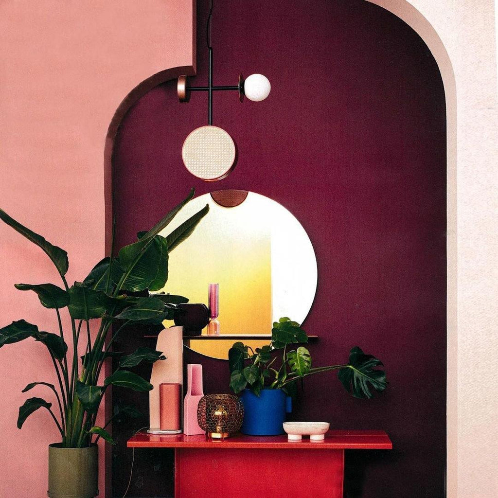Clérachic pendant hanging in a burgundy archway beside a console table with vases, plants and a round mirror.