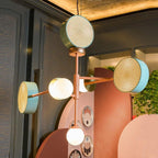 Clérachic chandelier hanging in a dark-panelled lounge, its cane drums and lit glass globe glowing against timber cabinetry and trailing greenery.