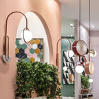 Several Clérachic drum-and-globe pendants lit above a plant-filled hallway with an arched doorway and patterned tiled wall.