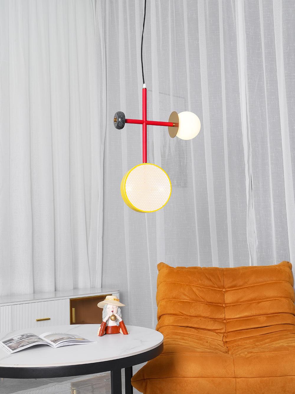 Clérachic pendant with a red rod, dark bead cap and yellow-rimmed drum hanging over a round table, sheer curtains and an orange chair behind.