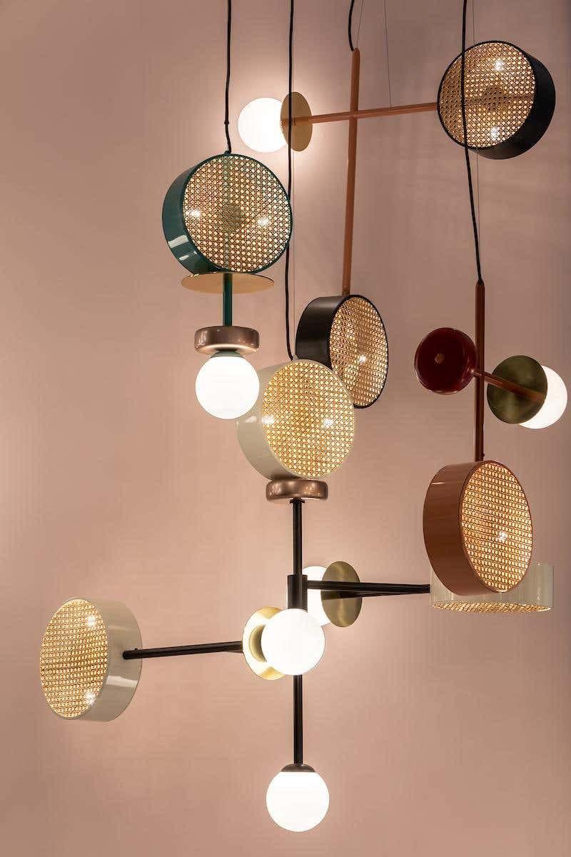 Cluster of several Clérachic drum-and-globe pendants suspended together against a plain blush studio wall.