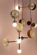 Cluster of several Clérachic drum-and-globe pendants suspended together against a plain blush studio wall.