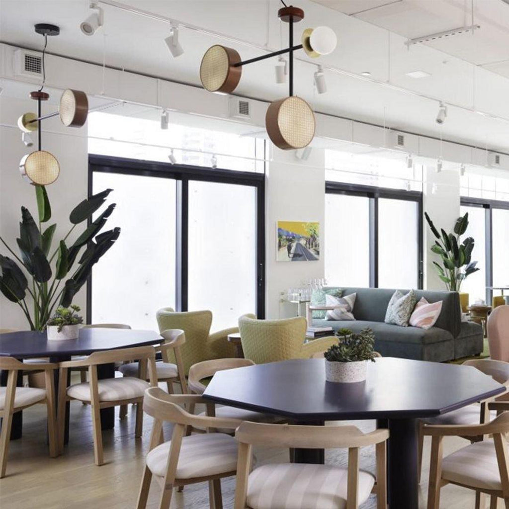 Several Clérachic drum-and-globe pendants lit above a showroom dining area furnished with sofas and chairs.