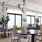 Several Clérachic drum-and-globe pendants lit above a showroom dining area furnished with sofas and chairs.