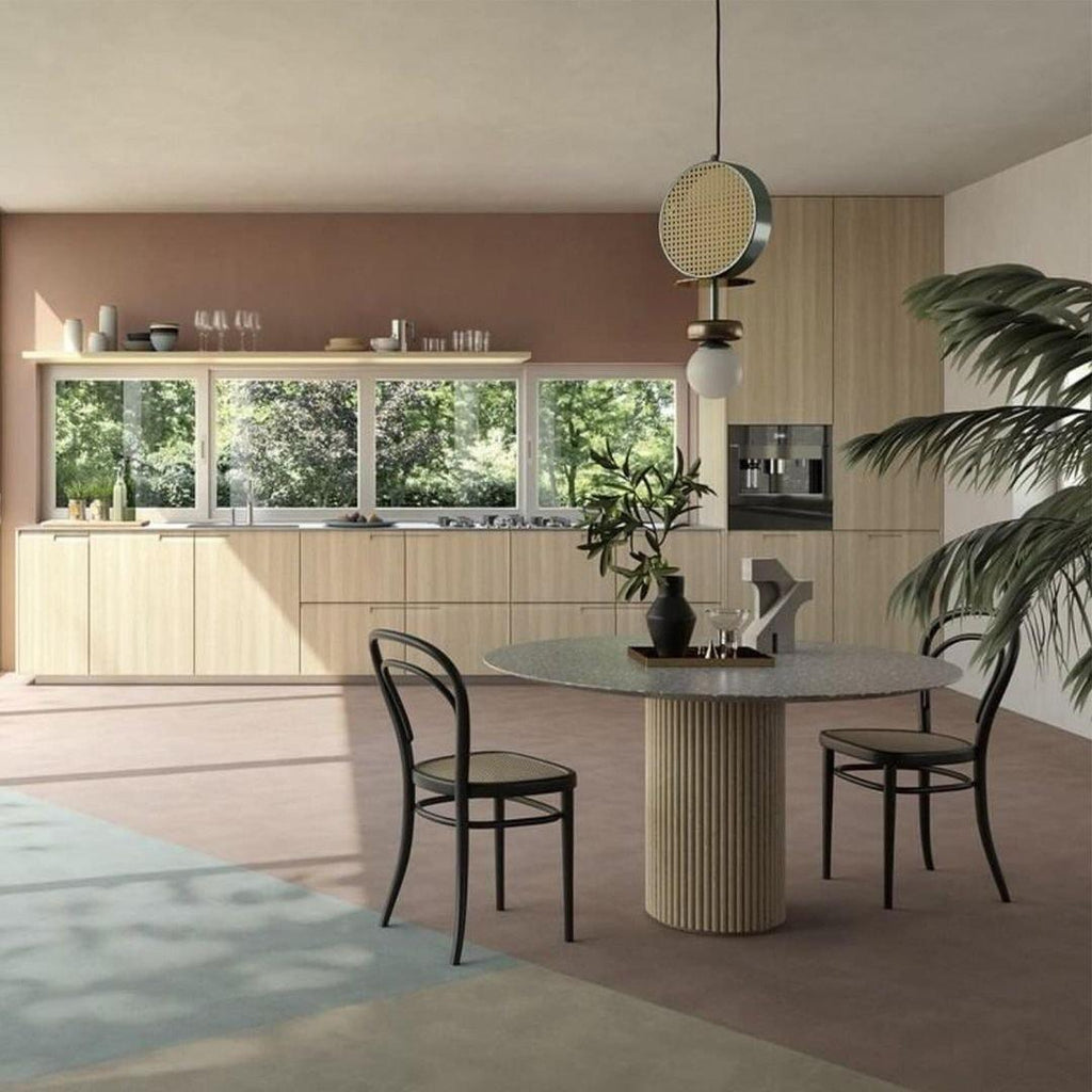 Clérachic drum pendant hanging over a round dining table in a wood-toned kitchen, with a garden view through the window.