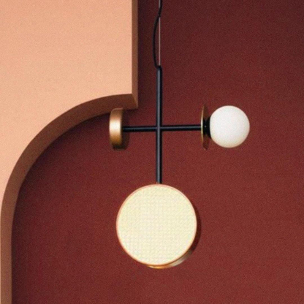 Clérachic pendant with a black cross-rod, one cane drum and one opal glass globe, hanging against a deep burgundy wall.