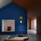 Clérachic pendant hanging alone against a deep blue architectural wall, with a red upholstered chair and built-in shelf below.