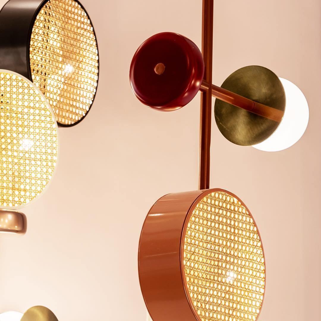 Cluster of copper cane drum shades and an opal glass globe on a Clérachic chandelier's brass arms, photographed close against a soft pink blur.