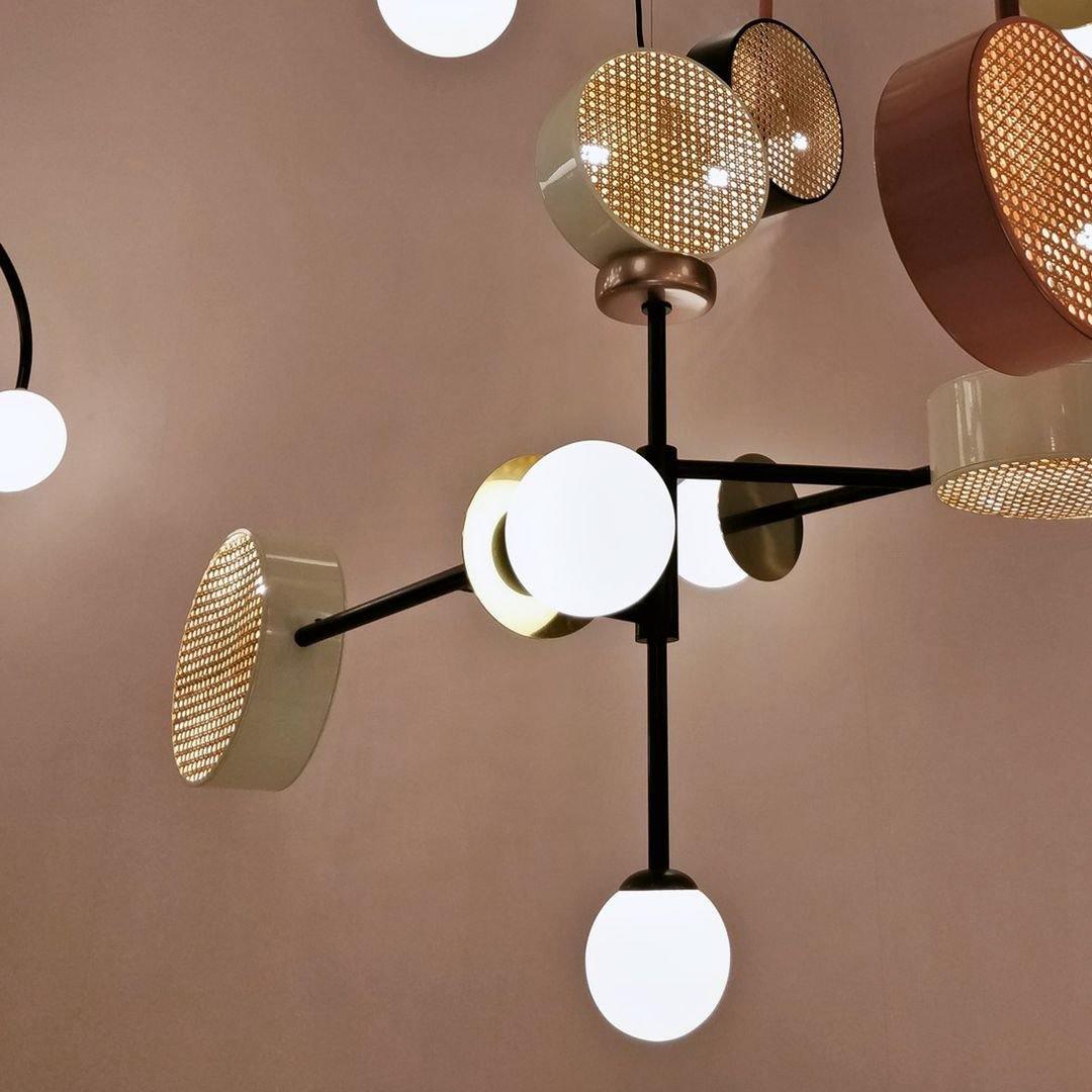 Close cluster of several cane drum shades in copper and cream on a Clérachic chandelier's black frame, with globes visible between them.