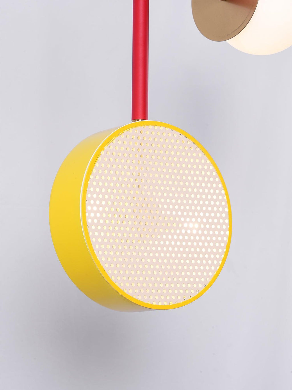 Close-up of a Clérachic pendant's yellow-rimmed cane drum shade and brass disc against a plain grey background.