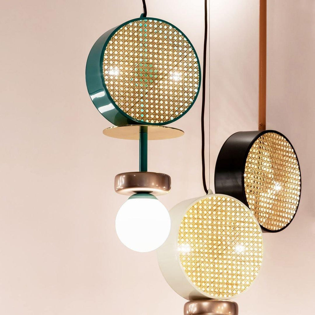 Close cluster of a Clérachic chandelier's drum shades in teal, black and gold-rimmed cane, photographed above a potted plant.