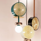 Close cluster of a Clérachic chandelier's drum shades in teal, black and gold-rimmed cane, photographed above a potted plant.