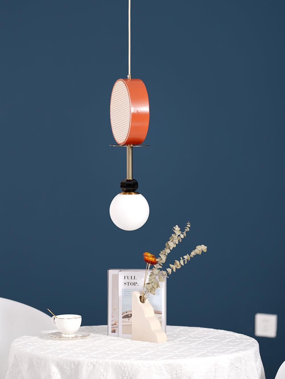 Clérachic pendant hanging above a small round table set with a teacup and vase against a teal wall.