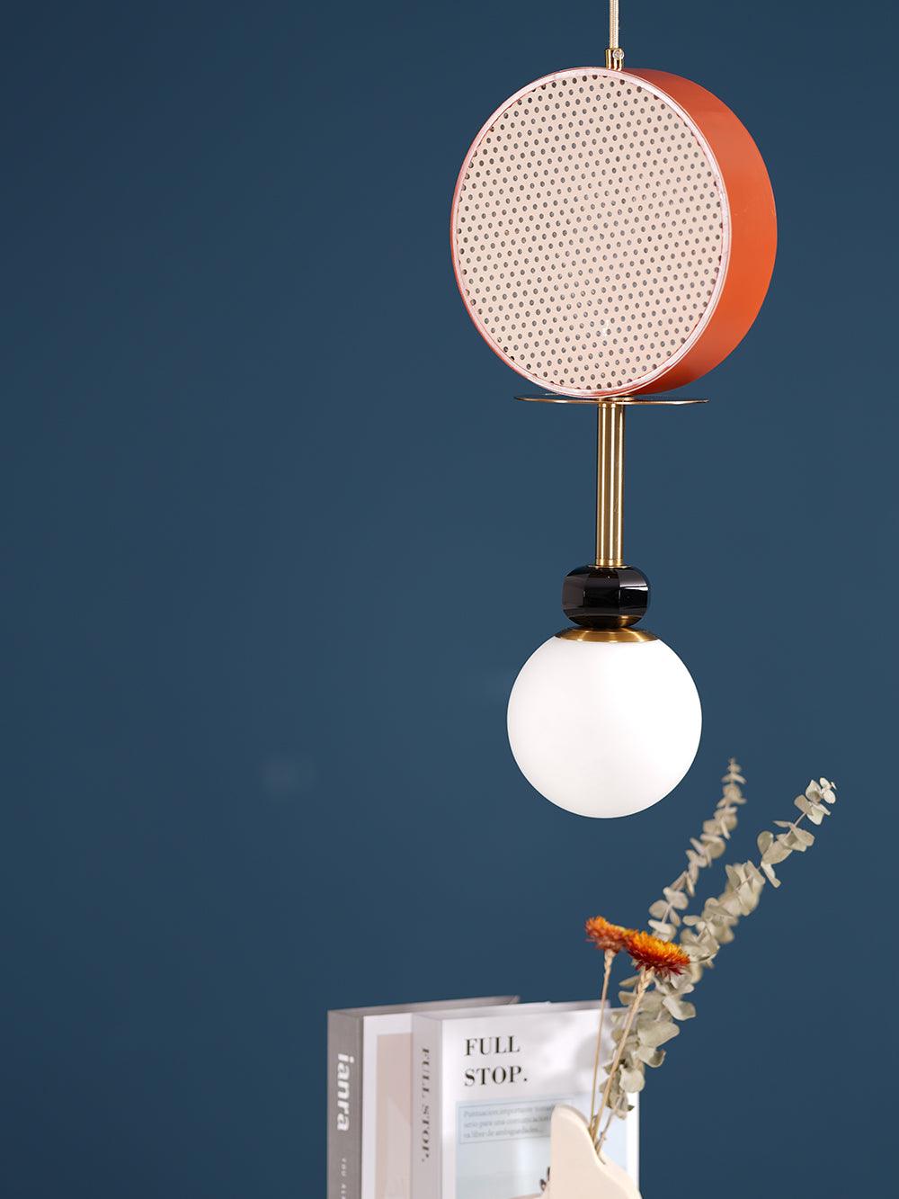 Clérachic pendant hanging against a teal curtain backdrop, with dried flowers and stacked books on the table below.