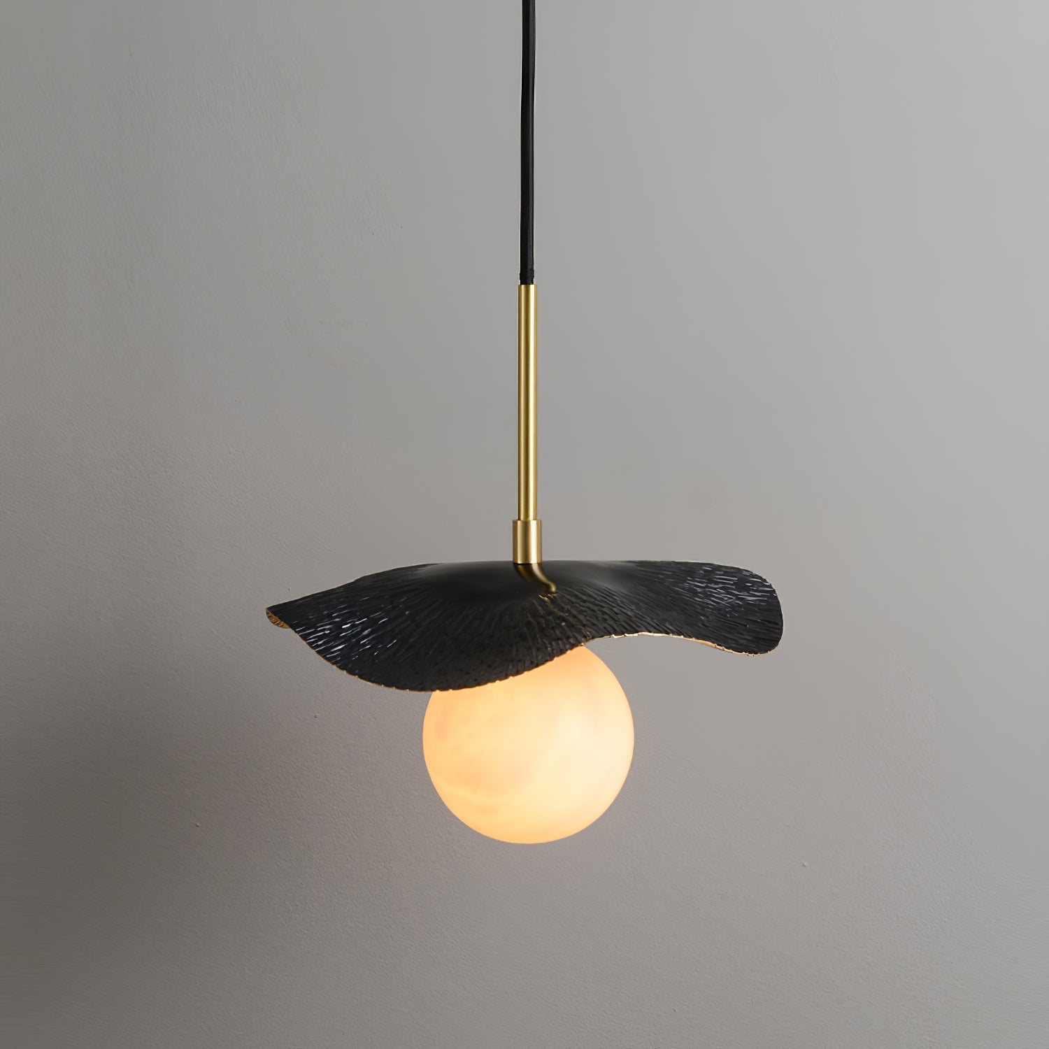The black-finish version of the pendant, its matte leaf shade lit from below by the alabaster globe