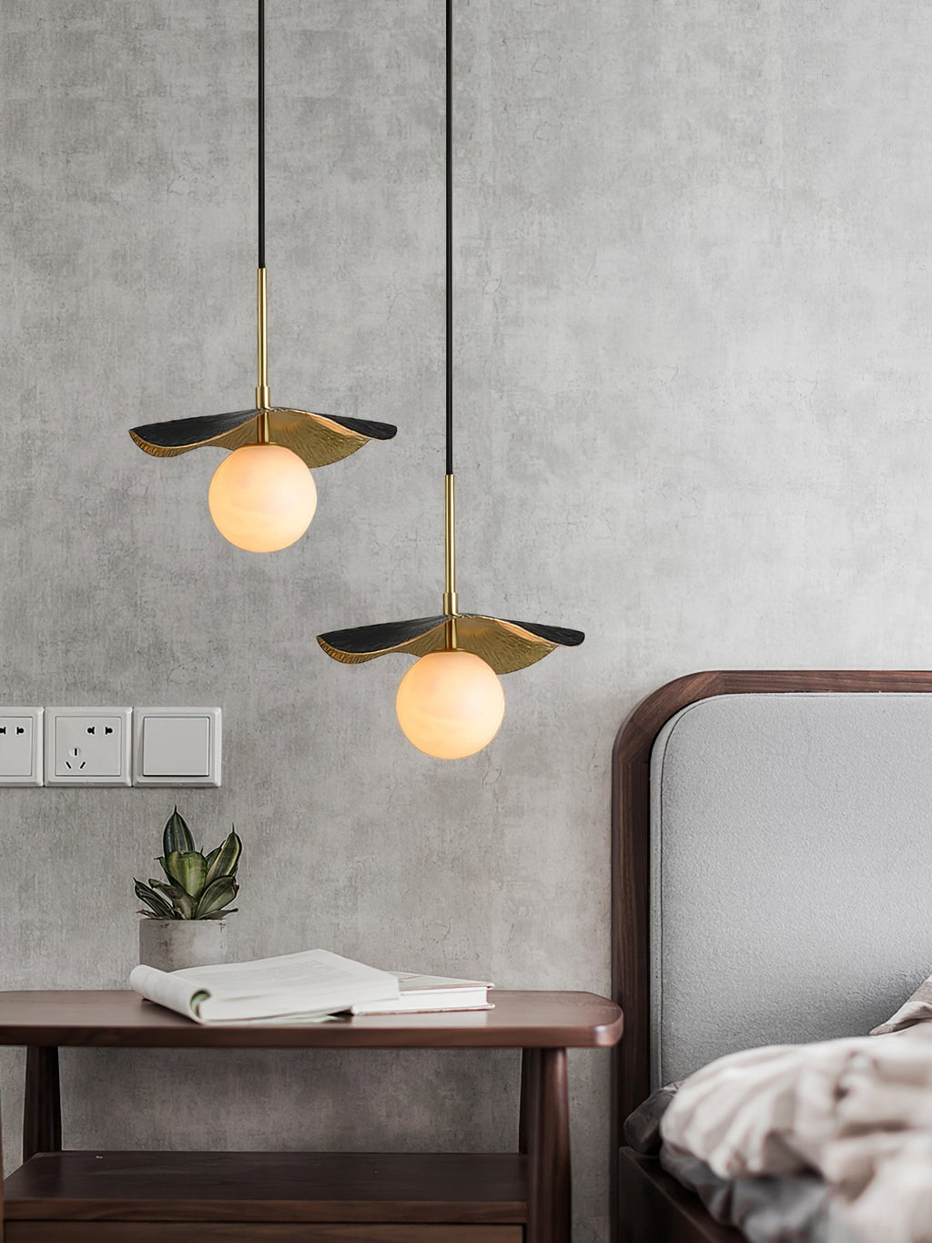 Two pendants hung at staggered heights beside a bed, lighting a walnut nightstand and concrete wall