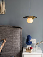 Close bedside view of the lit pendant beside a blue bust and perfume on a white nightstand