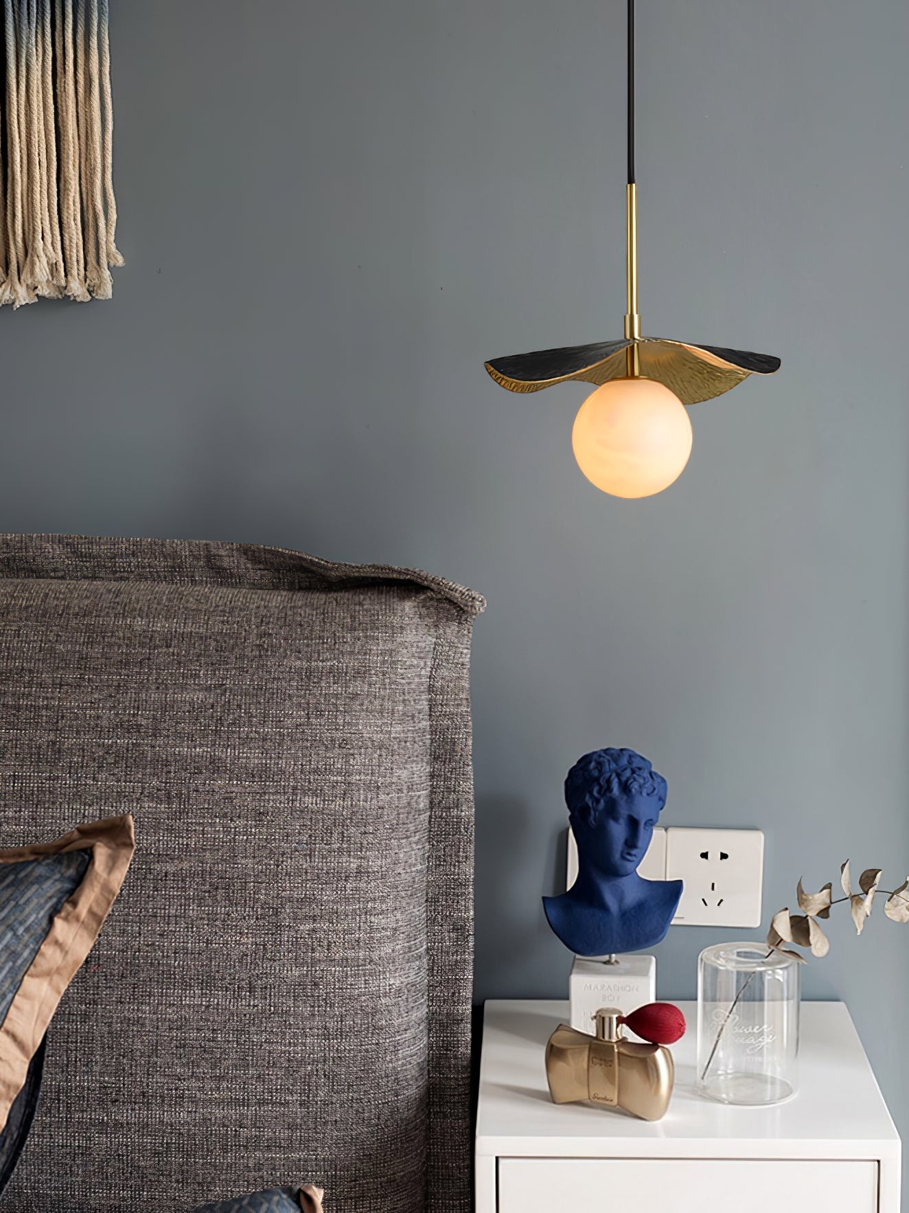 Close bedside view of the lit pendant beside a blue bust and perfume on a white nightstand
