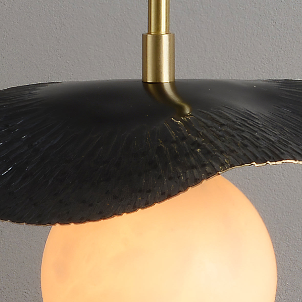 Detail of the black leaf shade's top surface where the slim brass stem meets the curved metal