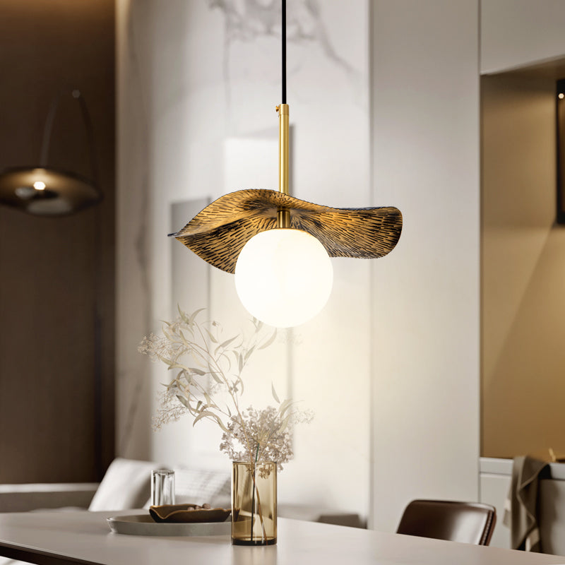 The pendant lit above a dining table, its brass shade catching light beside a vase of blossom