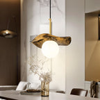 The pendant lit above a dining table, its brass shade catching light beside a vase of blossom