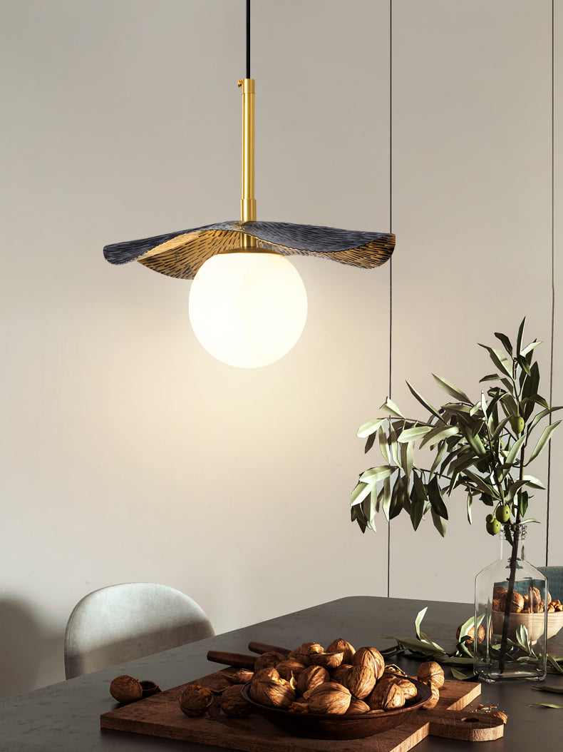 The pendant lit above a dark dining table set with walnuts and an olive branch