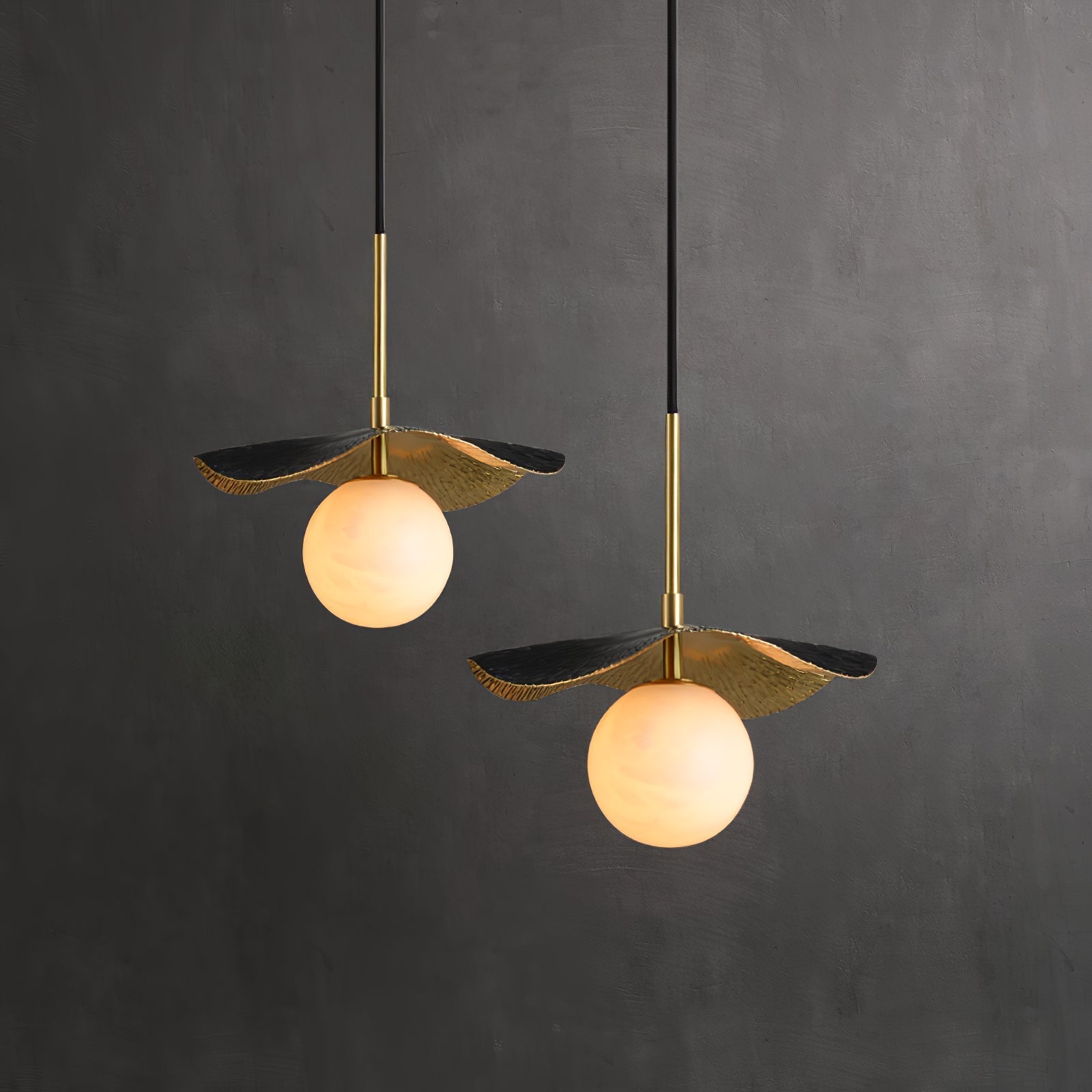 Two pendants against a charcoal studio wall, brass shades and alabaster globes shown at two heights
