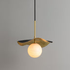 The brass pendant lit against a grey wall, warm light glowing through the veined alabaster globe