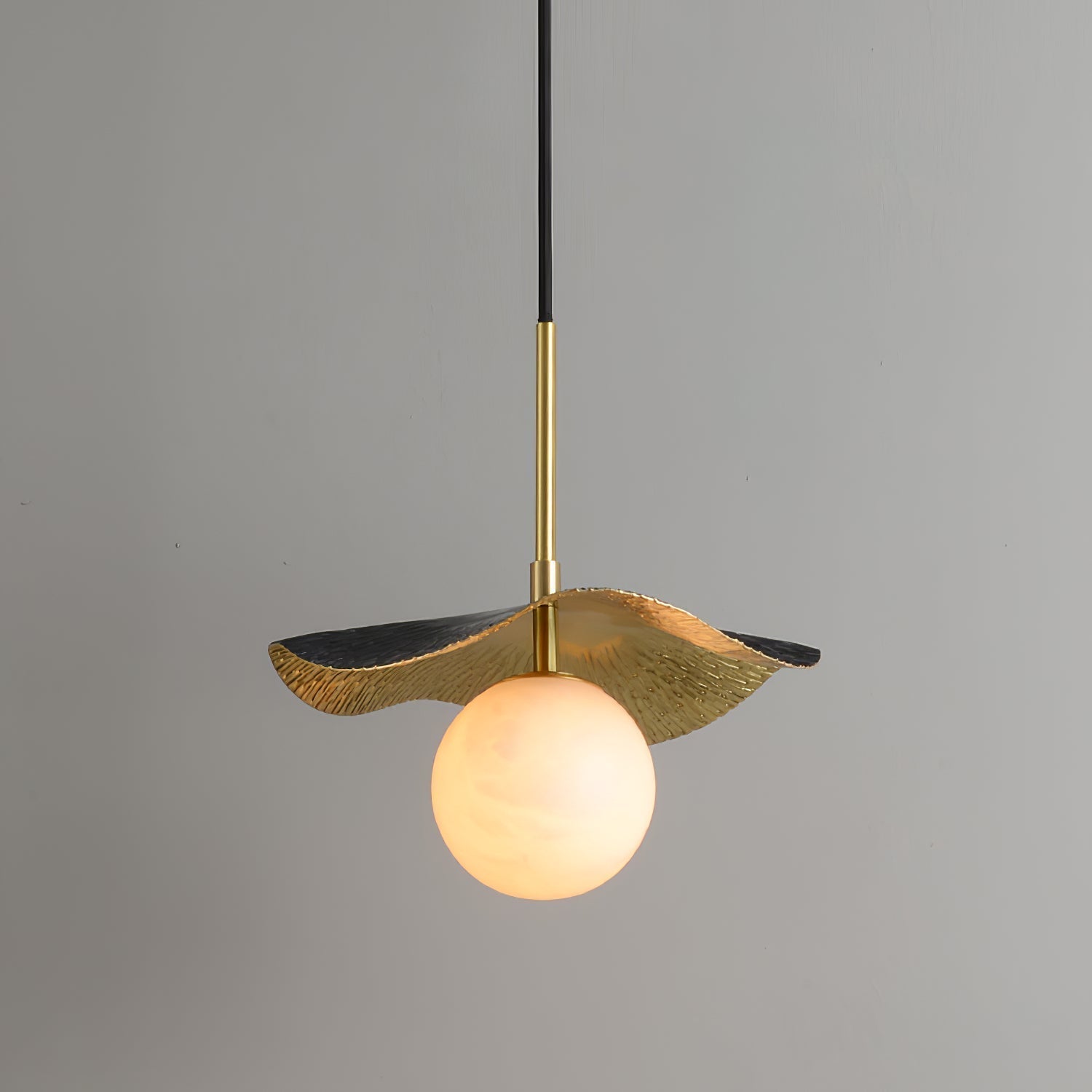 The brass pendant lit against a grey wall, warm light glowing through the veined alabaster globe