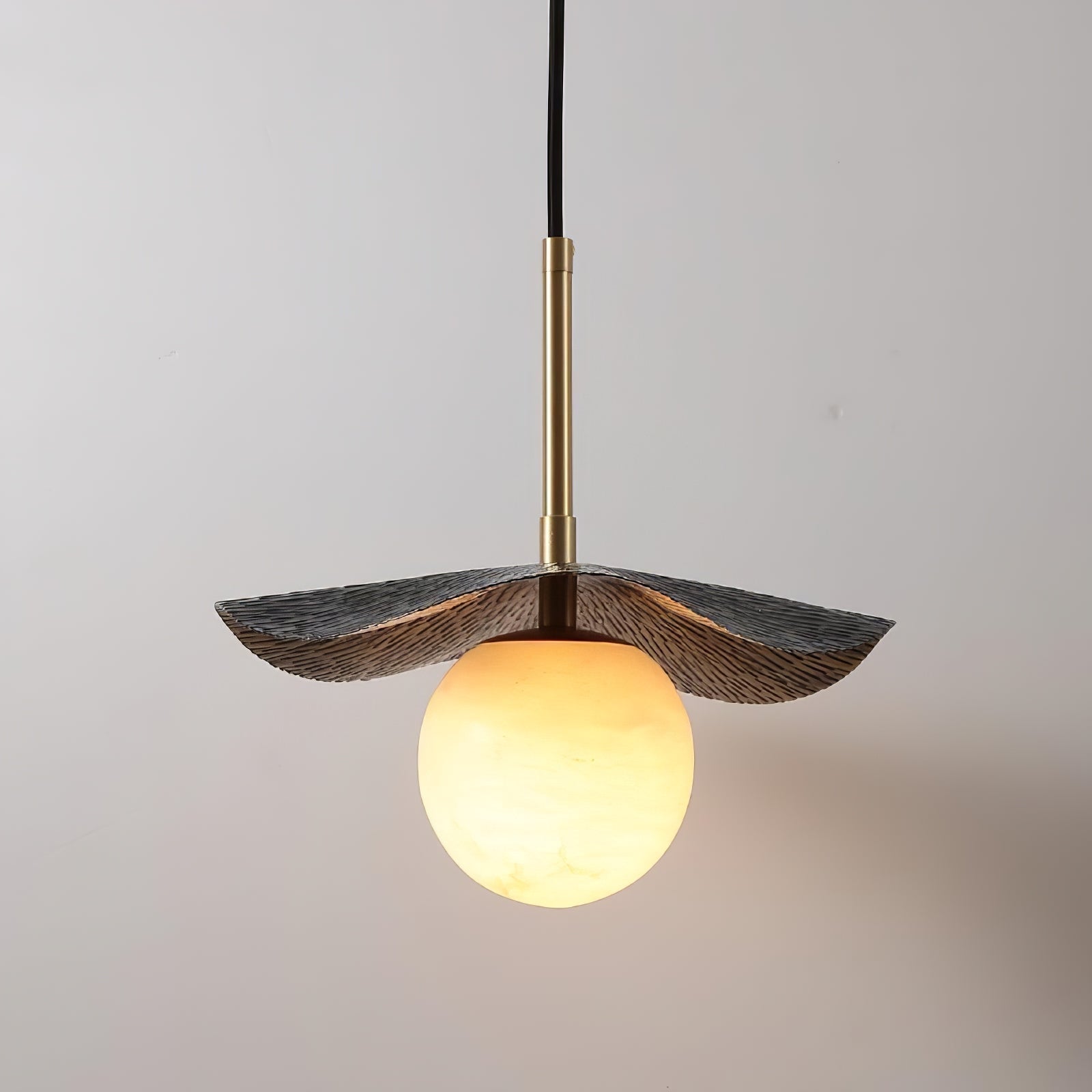 Low angle on the pendant showing the ridged underside of the brass shade and the amber-lit globe