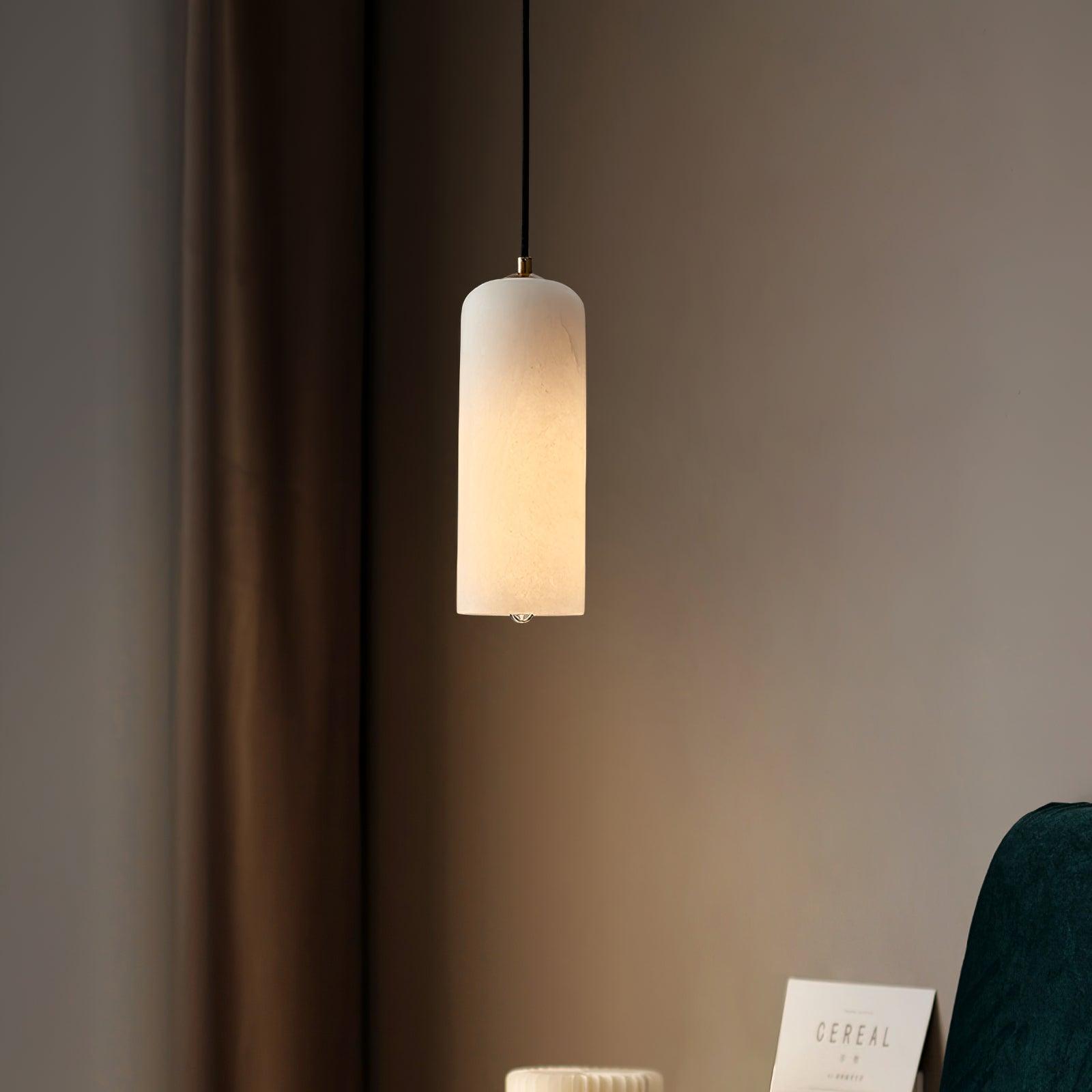 Hecate pendant lit beside a taupe curtain, its warm glow falling over a magazine and green chair below.