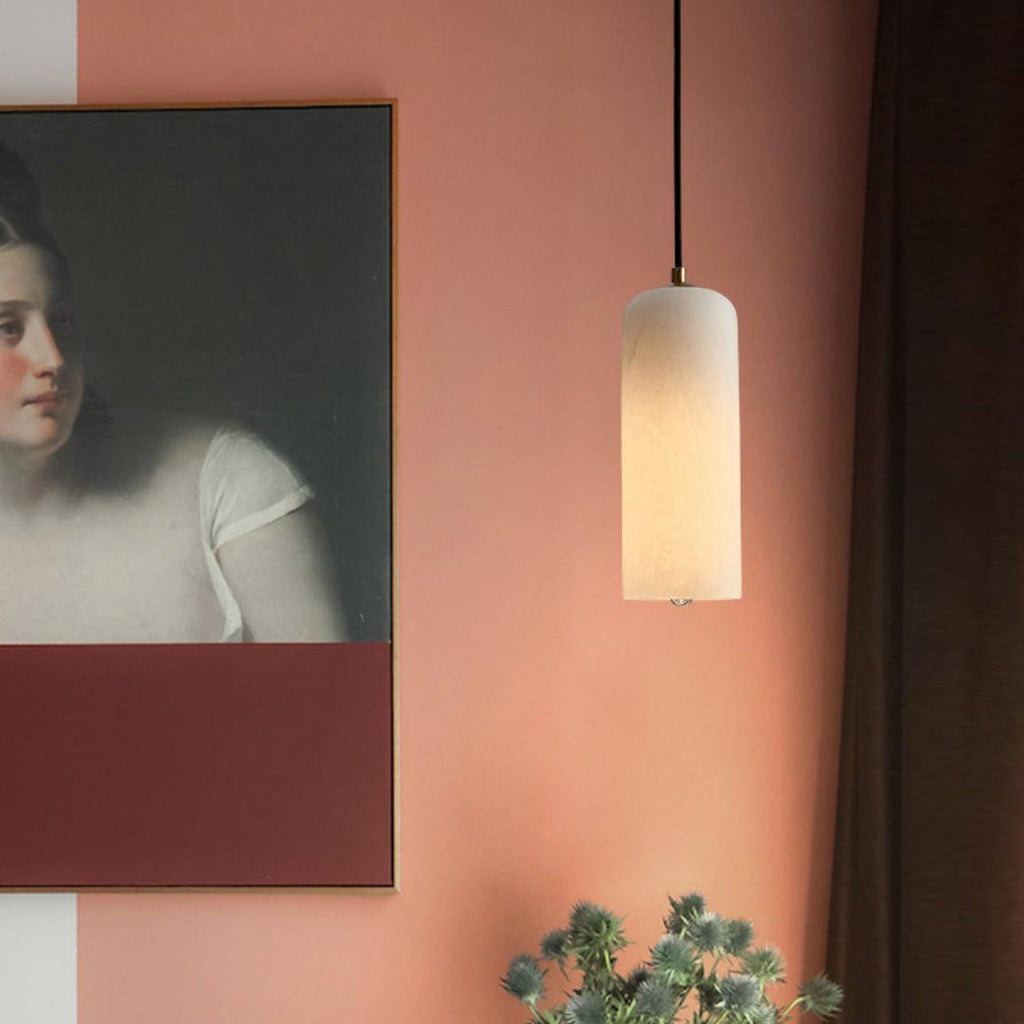 Hecate alabaster pendant lit beside a framed portrait on a terracotta wall above dried thistles.