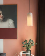 Zashayra pendant lit against a terracotta wall beside a framed portrait and a vase of blue thistles.