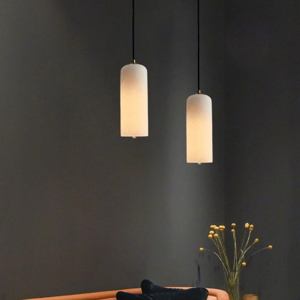 A pair of Hecate alabaster pendants glowing at staggered heights above a sofa on a charcoal wall.