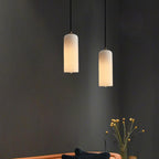 A pair of Hecate alabaster pendants glowing at staggered heights above a sofa on a charcoal wall.
