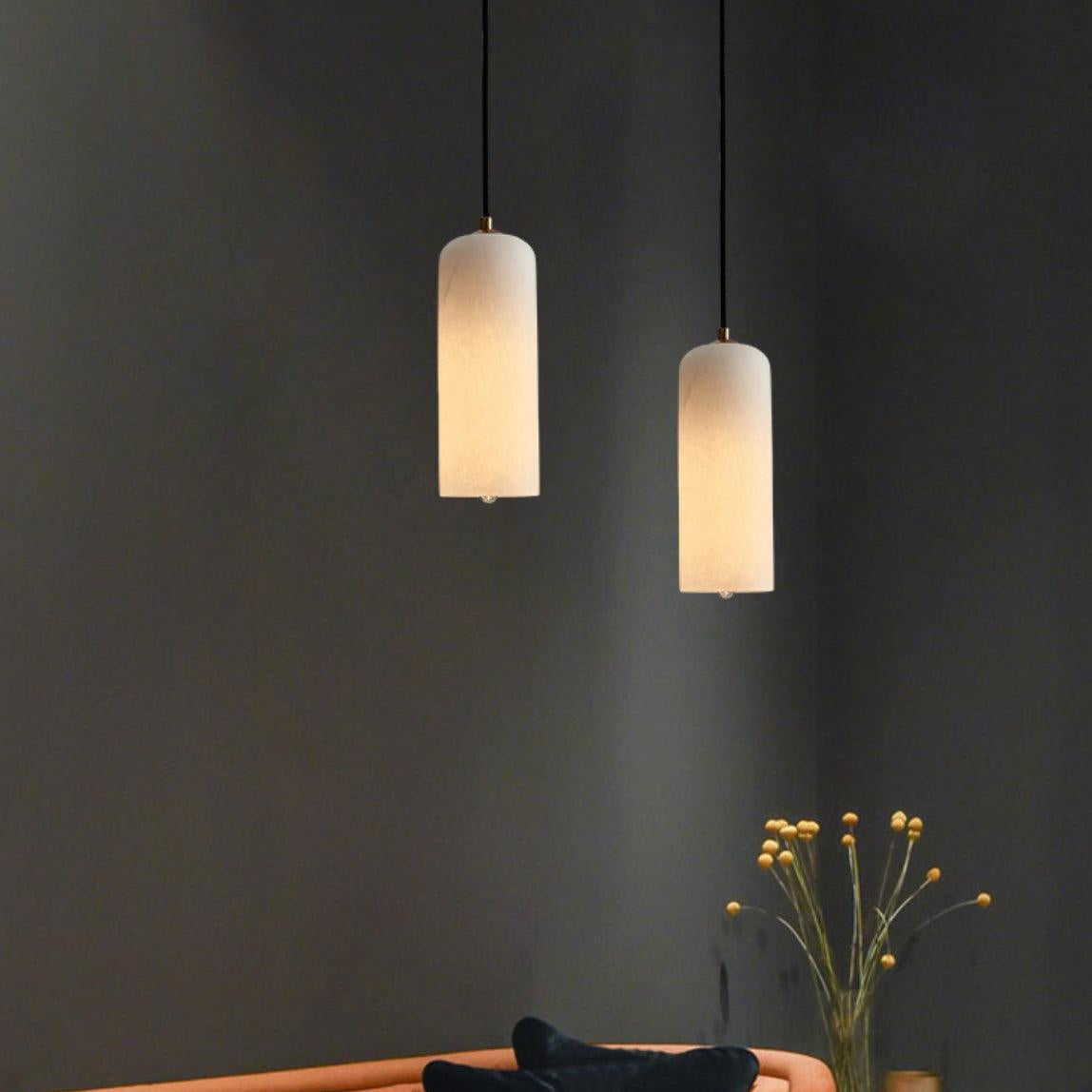 A pair of Hecate alabaster pendants glowing at staggered heights above a sofa on a charcoal wall.